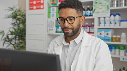 Sticker - A young adult black man with glasses and a beard working on a computer at a pharmacy store