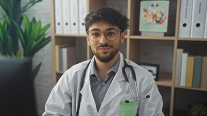 Canvas Print - A handsome arab man in medical attire with a stethoscope posing confidently in a clinic interior.