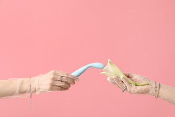 Wall Mural - Female hands in laced gloves with vibrator and lily flower on pink background