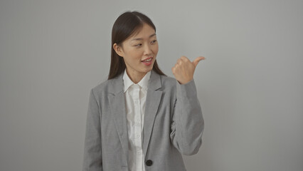 Wall Mural - A young asian woman in business attire smiling and gesturing with her thumb over an isolated white background.