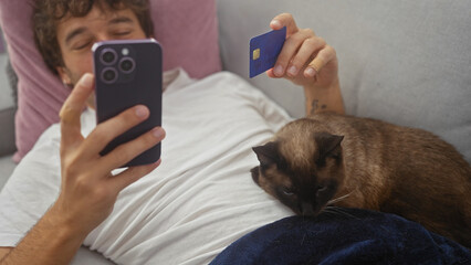 Poster - Man lounging with cat using smartphone and credit card indoors