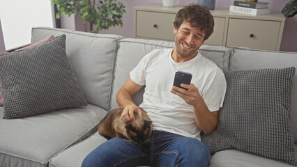 Sticker - A smiling young hispanic man petting a cat while using a smartphone on a sofa in a cozy living room