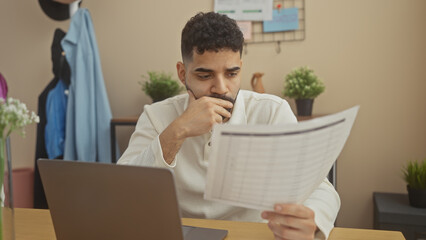 Wall Mural - Concentrated hispanic man analyzing documents in a modern apartment office setup.