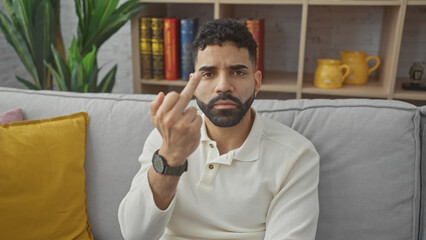 Sticker - A young hispanic man gestures disapprovingly with his middle finger while sitting in a cozy home living room.