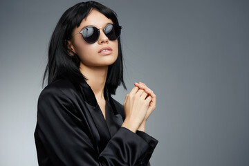 Portrait of a beautiful woman in a black suit and sunglasses against a gray background, exuding confidence and elegance, perfect for fashion and professionalthemed projects