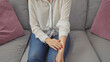 © Krakenimages.com - A young woman sitting on a grey sofa indoors touches her wrist, showcasing her red nails and casual style.