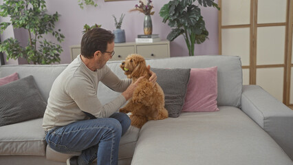 Poster - A middle-aged man affectionately pets a poodle on a sofa in a cozy living room setting, creating a homely scene.