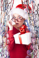 amazed fun christmas woman wears red eyeglasses and santa hat. girl show gift box with bow image for