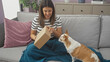 © Krakenimages.com - A smiling woman sits on a couch at home, showing a box to an attentive chihuahua, in a serene living room.