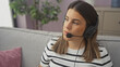 © Krakenimages.com - A focused young woman with a headset works remotely from her cozy living room couch.