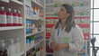 © Krakenimages.com - A female pharmacist in a white coat selects medicines inside a well-stocked pharmacy with shelves of products.