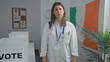© Krakenimages.com - A young hispanic woman in a white lab coat stands in an electoral college room in ireland, with voting booths and an irish flag in the background.