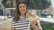 © Krakenimages.com - A young hispanic woman holding her chihuahua dog in an urban park smile warmly in this outdoor city street scene.