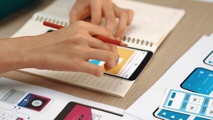 Startup company employee planning for user interface prototype for mobile application or website in office with model of program on desk. UX UI designer consider user friendly interface plan. Synergic