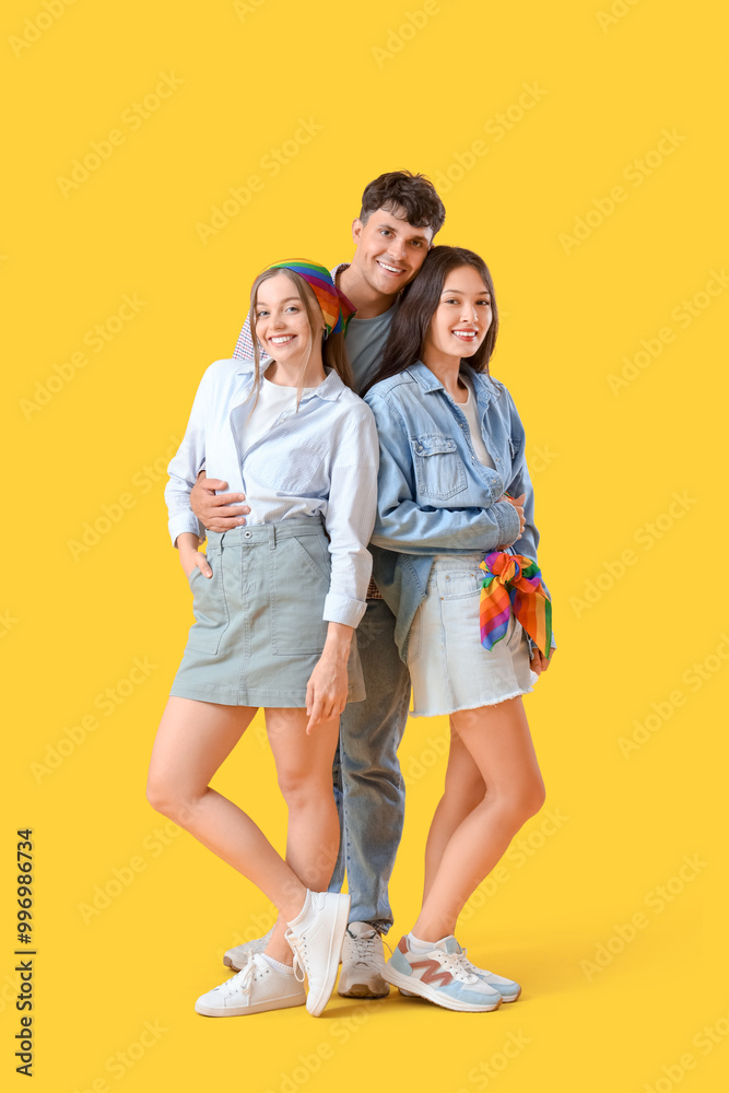 Young man hugging two women on yellow background. Polyamory concept