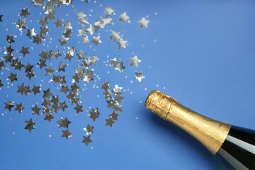 Wall Mural - Bottle of sparkling wine and confetti on blue background, top view