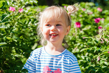 Little toddler child girl walks in a blooming green garden in summer.