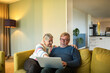 © Marko Geber - Happy senior couple sitting on couch using laptop together