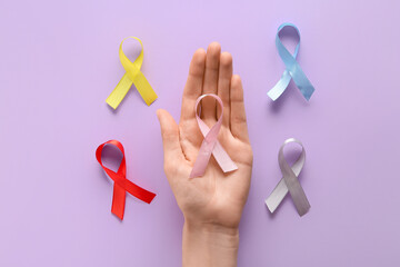 Wall Mural - Female hand with colorful ribbons on lilac background. World Cancer Day