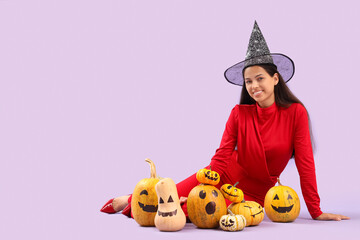 Poster - Young woman in witch hat and with Halloween pumpkins on lilac background