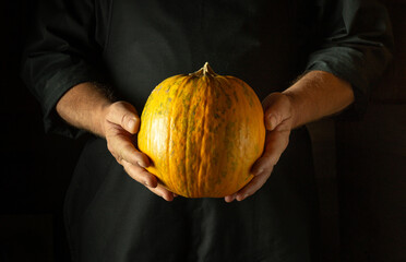 Canvas Print - Chef holding a large ripe pumpkin before cooking or baking it in the kitchen. Low key concept of a fruit diet or cooking a national dish