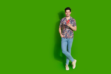 Poster - Full size photo of smart guy dressed print shirt jeans look at smartphone stand near empty space isolated on green color background