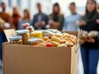 © Myimages - Cardboard box filled with canned goods and nonperishable food, out of focus people in the background - Emergency Food Stock, Humanitarian Aid, SNAP Assistance Program