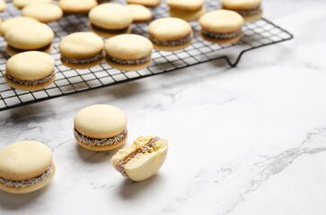 Cornstarch alfajores filled with dulce de leche on a black rack on a white background. 