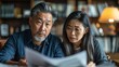© Pat J. - Asian couple looking anxious and sad, holding bills and discussing financial issues at home
