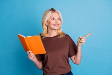 Photo of adorable positive retired woman wear trendy brown clothes recommend book empty space isolated on blue color background