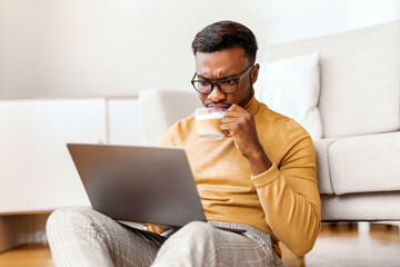 Aufkleber - Busy Black Entrepreneur Guy Using Laptop Having Morning Coffee And Reading Business News Online Sitting On Floor At Home