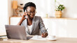 © Prostock-studio - Black Millennial Businesswoman Talking On Cellphone And Taking Notes While Working On Laptop In Modern Office, Selective Focus