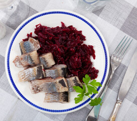 Pieces of chopped herring with grounded beetroot served on plate. Fish refreshment on table.