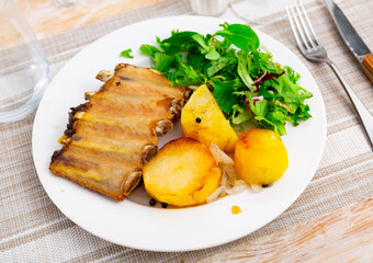 Portion of grilled pork ribs with roasted potatoes served with green salad in plate. Spanish dish