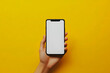 © dadakko - 黄色い背景にスマートフォンを持つ手のクローズアップ