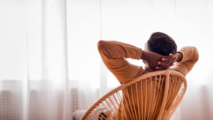 Poster - Relax. African American Man Sitting On Modern Chair Back To Camera Looking In Window At Home. Selective Focus