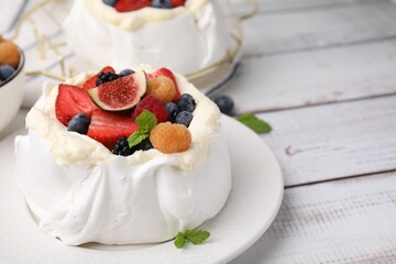 Pavlova cake (meringue dessert) with whipped cream, fresh berries, fig and mint on white wooden table, closeup