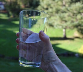 a hand holding out a drink of water in a clear glass outside