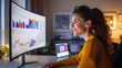 © Jirawatfoto - woman is smiling while working on computer, analyzing colorful graphs and charts on large monitor. warm lighting creates cozy atmosphere, enhancing her focused expression