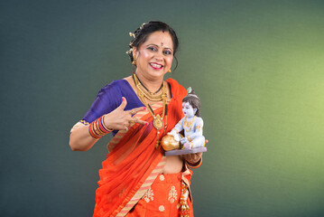 Traditional Indian woman wearing saree posing with God Lord Krishna idol