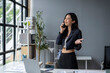 © apichat - A woman is talking on her cell phone in a room with a desk and a potted plant