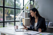 © apichat - A woman is sitting at a desk with a laptop and a cell phone