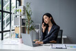© apichat - A woman is talking on her cell phone while sitting at a desk