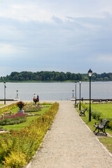 
Flowers and street lamps in the city park along the roadside on the background of the river