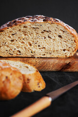 Fresh grain bread next to cut pieces on a wooden board on a dark background