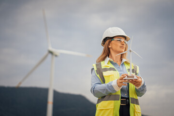 Poster - A female engineer proudly holding a wind turbine model at a renewable energy site, showcasing her commitment to sustainable practices and innovation in engineering within the construction industry