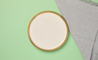 Round ceramic empty white plate and gray linen kitchen towel on green background, top view