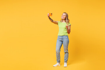 Wall Mural - Full body young happy blonde woman wear green t-shirt casual clothes doing selfie shot on mobile cell phone post photo on social network isolated on plain yellow orange background. Lifestyle concept.