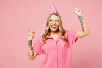 Poster - Young overjoyed excited woman wear shirt cone hat celebrating birthday holiday hold in hand blowing pipe do winner gesture isolated on plain pastel pink background studio portrait. Lifestyle concept.