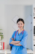 © Kritdanai - Confident Female Doctor: Portrait of a smiling Asian female doctor in scrubs with arms crossed, showcasing confidence and professionalism in a medical setting. 